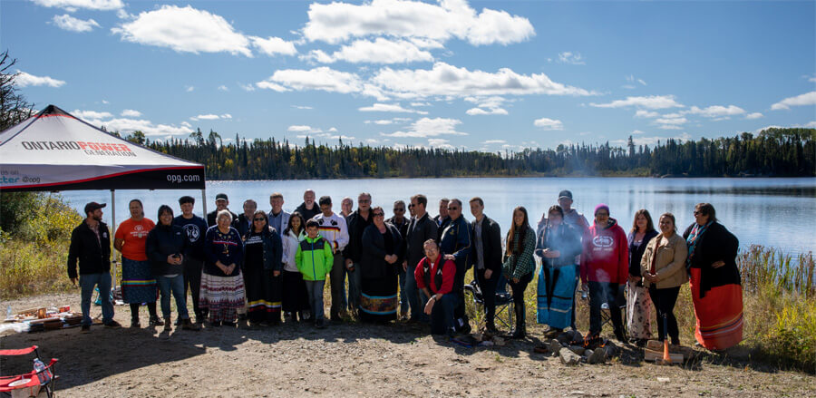 先住民に縁のある湖に集まった先住民と開発企業の社員の写真