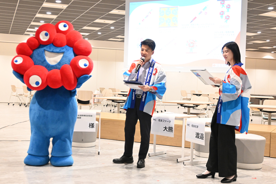 From right, Ms. Riho Watanabe of Sumitomo Chemical and Mr. Takashi Okuma of Sumitomo Pharma, who served as MCs, and MYAKU-MYAKU, the official character.